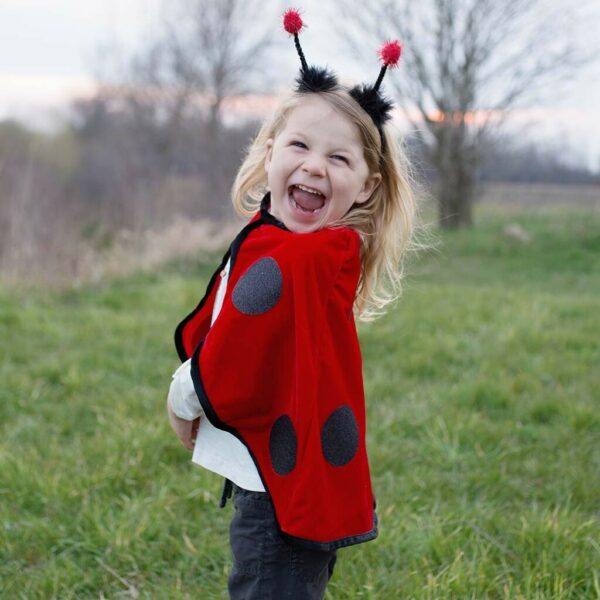 Cape de coccinelle rouge à pois noir portée par un enfant qui porte le serre-tête avec des antennes à pompons