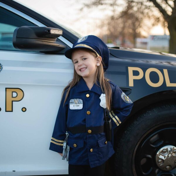 une petite fille porte le déguisement de pompier devant une voiture de police